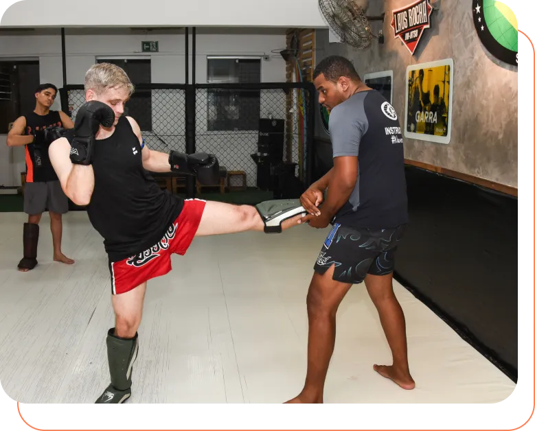 Aluno treinando chute de Muay Thai com o professor segurando o aparador